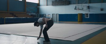 Movie still from “Alps” (2011), directed by Yorgos Lanthimos – A man standing on one foot in a gym; Medium shot, Low angle