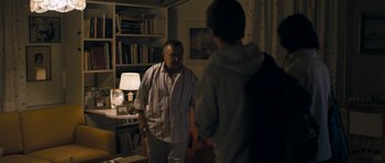 Movie still from “Alps” (2011), directed by Yorgos Lanthimos – Two men standing in a living room talking to each other; Medium shot, Over the shoulder angle