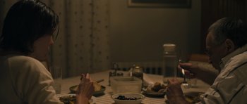 Movie still from “Alps” (2011), directed by Yorgos Lanthimos – A person sitting at a table with a bowl of food; Medium shot, Over the shoulder angle