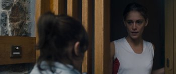 Movie still from “Alps” (2011), directed by Yorgos Lanthimos – A man and a woman are standing next to each other in front of a wooden wall; Medium shot, Over the shoulder angle