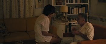 Movie still from “Alps” (2011), directed by Yorgos Lanthimos – A woman sitting on a chair next to a man; Medium shot, High angle
