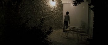 Movie still from “Alps” (2011), directed by Yorgos Lanthimos – A person standing in front of an open door; Wide shot, Low angle