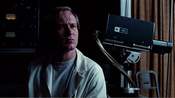 Movie still from “Altered States” (1980), directed by Ken Russell – A man sitting in front of a video camera in a room; Close Up shot, Low angle