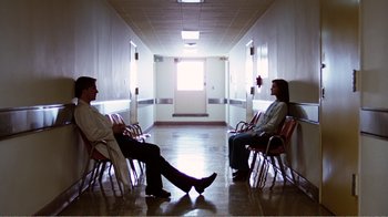 Movie still from “Altered States” (1980), directed by Ken Russell – Two people sitting in chairs in a hospital hallway; Wide shot, Low angle