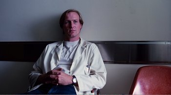 Movie still from “Altered States” (1980), directed by Ken Russell – A man in a white lab coat sitting in a chair; Medium shot, Low angle
