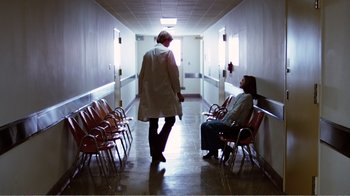 Movie still from “Altered States” (1980), directed by Ken Russell – Two people sitting in chairs in a hospital hallway; Wide shot, Low angle