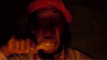 Movie still from “Altered States” (1980), directed by Ken Russell – An old man wearing a red hat is holding a wooden spoon; Close Up shot, Low angle