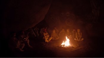 Movie still from “Altered States” (1980), directed by Ken Russell – A group of people sitting around a fire in a cave; Wide shot, High angle