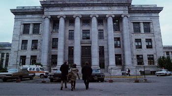 Movie still from “Altered States” (1980), directed by Ken Russell – Three people are standing in front of a large building; Extreme Wide shot, Low angle