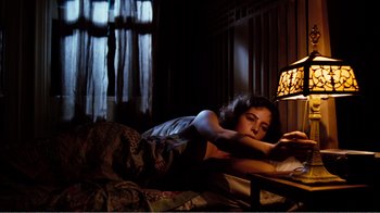 Movie still from “Altered States” (1980), directed by Ken Russell – A woman laying on a bed looking at a book; Medium shot, Overhead angle