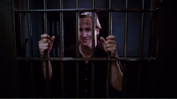 Movie still from “Altered States” (1980), directed by Ken Russell – A man in black shirt behind a metal fence; Medium shot, High angle