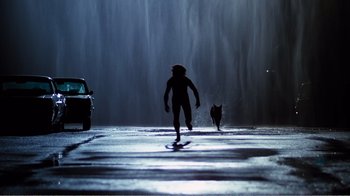 Movie still from “Altered States” (1980), directed by Ken Russell – A person and a cat walking down a street; Wide shot, Low angle
