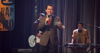 Movie still from “Alvin and the Chipmunks: The Squeakquel” (2009), directed by Betty Thomas – A man in a suit and tie holding a microphone; Medium shot, Over the shoulder angle