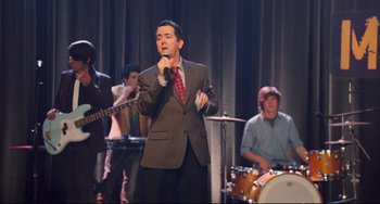 Movie still from “Alvin and the Chipmunks: The Squeakquel” (2009), directed by Betty Thomas – A man in a suit and tie singing into a microphone; Medium shot, Over the shoulder angle