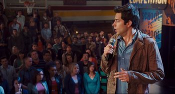 Movie still from “Alvin and the Chipmunks: The Squeakquel” (2009), directed by Betty Thomas – A man standing in front of a crowd holding a microphone; Medium shot, Over the shoulder angle