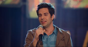 Movie still from “Alvin and the Chipmunks: The Squeakquel” (2009), directed by Betty Thomas – A man holding a microphone while wearing a brown jacket; Close Up shot, Over the shoulder angle