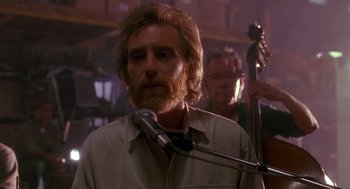 Movie still from “Always” (1989), directed by Steven Spielberg – A man with long hair and a goatee standing in front of a microphone; Close Up shot, Over the shoulder angle
