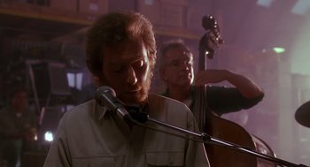 Movie still from “Always” (1989), directed by Steven Spielberg – A man with a beard and a microphone in front of two other men; Medium shot, Over the shoulder angle