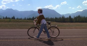 Movie still from “Always” (1989), directed by Steven Spielberg – A man riding a bike down the middle of the road; Wide shot, Low angle
