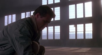 Movie still from “Always” (1989), directed by Steven Spielberg – A man in military fatigues kneeling down in front of a building; Medium shot, Low angle