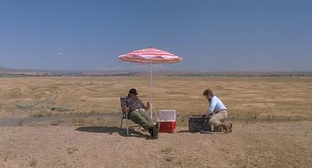 Movie still from “Always” (1989), directed by Steven Spielberg – Two men sitting under an umbrella in the middle of a field; Extreme Wide shot, High angle