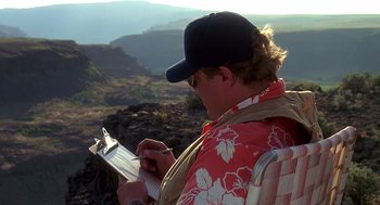 Movie still from “Always” (1989), directed by Steven Spielberg – A man is writing on a clipboard while sitting on a chair; Medium shot, Over the shoulder angle