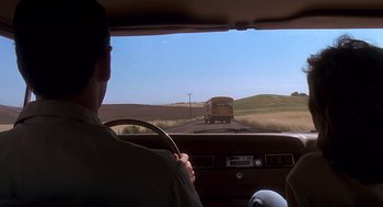 Movie still from “Always” (1989), directed by Steven Spielberg – A man driving a car on a road with a school bus in the background; Wide shot, Low angle