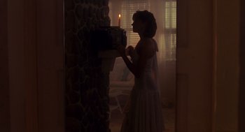 Movie still from “Always” (1989), directed by Steven Spielberg – A woman standing in front of a fireplace with a lit candle; Wide shot, Low angle