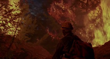 Movie still from “Always” (1989), directed by Steven Spielberg – A man with a backpack standing in front of a fire; Wide shot, Low angle