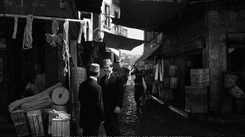 Movie still from “America America” (1963), directed by Elia Kazan – A black and white photo of two men walking down a street; Wide shot, Over the shoulder angle