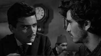 Movie still from “America America” (1963), directed by Elia Kazan – Two men in suits are talking to each other in front of a wall clock; Close Up shot, Over the shoulder angle