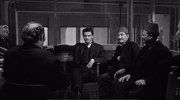 Movie still from “America America” (1963), directed by Elia Kazan – A group of men sitting next to each other on top of a bench; Wide shot, Over the shoulder angle