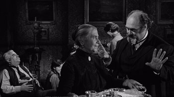 Movie still from “America America” (1963), directed by Elia Kazan – An older woman sitting at a table in front of an older man; Medium shot, Over the shoulder angle