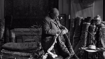 Movie still from “America America” (1963), directed by Elia Kazan – An old man is sitting in a room with a lot of rugs; Medium shot, High angle