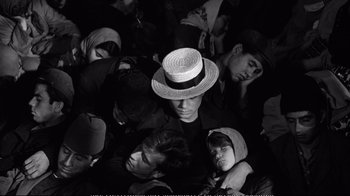 Movie still from “America America” (1963), directed by Elia Kazan – A group of people gathered around a man wearing a straw hat; Medium shot, Overhead angle
