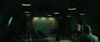 Movie still from “American Dharma” (2018), directed by Errol Morris – A group of chairs in a room with a map on the wall behind them; Extreme Wide shot, High angle