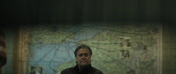 Movie still from “American Dharma” (2018), directed by Errol Morris – A man standing in front of a map of the world; Medium shot, High angle