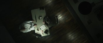Movie still from “American Dharma” (2018), directed by Errol Morris – Two people sitting at a table in a dark room; Wide shot, Overhead angle