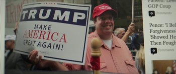 Movie still from “American Dharma” (2018), directed by Errol Morris – A man in a red hat holding up a sign; Medium shot, Low angle