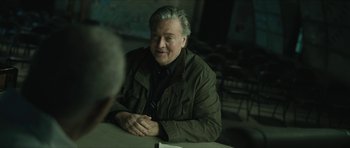 Movie still from “American Dharma” (2018), directed by Errol Morris – An older man sitting at a table in front of another man; Medium shot, Over the shoulder angle