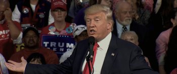 Movie still from “American Dharma” (2018), directed by Errol Morris – A man in a suit and tie speaking into a microphone in front of a crowd; Close Up shot, Over the shoulder angle