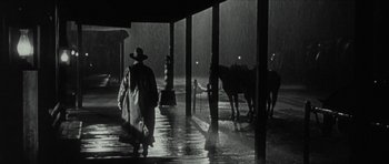Movie still from “American Dharma” (2018), directed by Errol Morris – A man walking down a rain covered street with a horse; Wide shot, Low angle