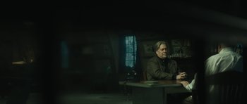 Movie still from “American Dharma” (2018), directed by Errol Morris – A man sitting at a table in front of a window; Medium shot, Low angle