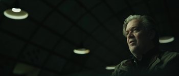 Movie still from “American Dharma” (2018), directed by Errol Morris – A man in a green shirt is in a dark room; Close Up shot, Over the shoulder angle