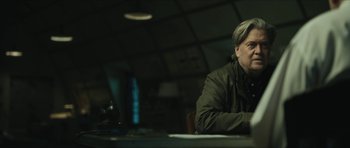 Movie still from “American Dharma” (2018), directed by Errol Morris – A man sitting at a table in front of a laptop; Medium shot, Low angle