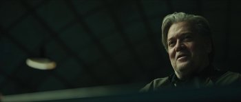 Movie still from “American Dharma” (2018), directed by Errol Morris – A man in a black shirt is smiling for the camera; Close Up shot, Over the shoulder angle