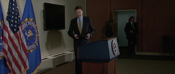 Movie still from “American Dharma” (2018), directed by Errol Morris – A man standing at a podium in front of a microphone; Wide shot, Low angle