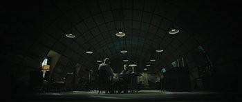 Movie still from “American Dharma” (2018), directed by Errol Morris – Two people are sitting at a table in a dark room; Extreme Wide shot, High angle