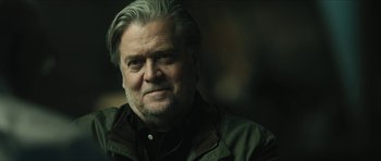 Movie still from “American Dharma” (2018), directed by Errol Morris – An older man with a gray beard is looking at the camera; Close Up shot, Over the shoulder angle