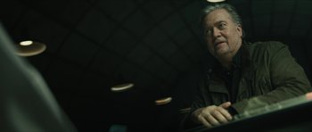 Movie still from “American Dharma” (2018), directed by Errol Morris – A man sitting at a table in a dark room; Close Up shot, Low angle